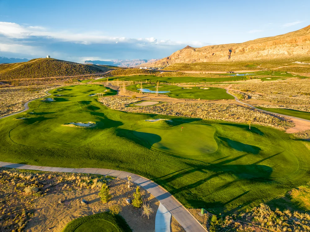 A green and sand bunkers at Copper Rock, with a winding cart path and desert cliffs beyond.