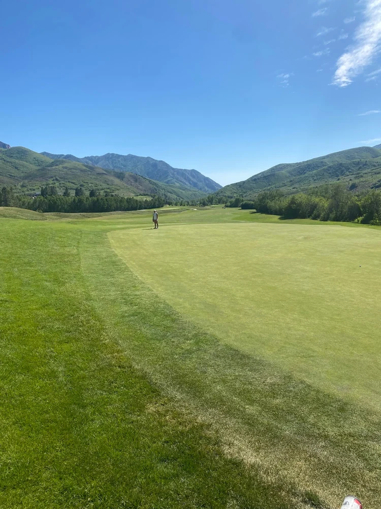 A golfer on a green at Mountain Dell, with tree-lined fairways and mountain ridges beyond.