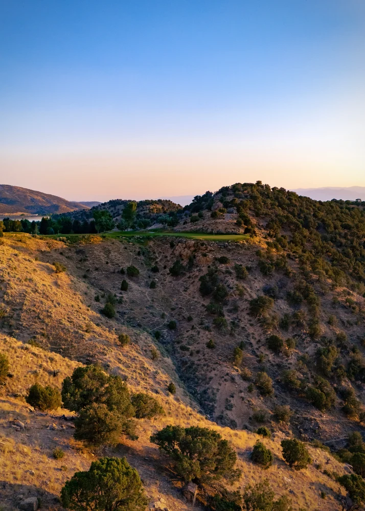 A green and flag at Palisade’s fourth hole across a steep, rocky ravine beneath a blue and pink sky.