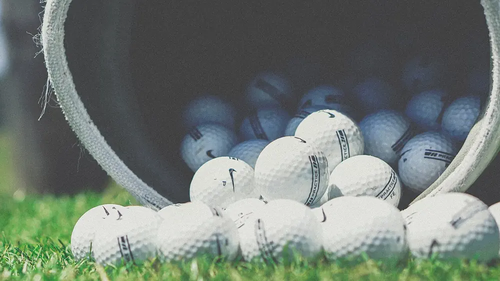 Practice golf balls spilling from a bucket onto grass