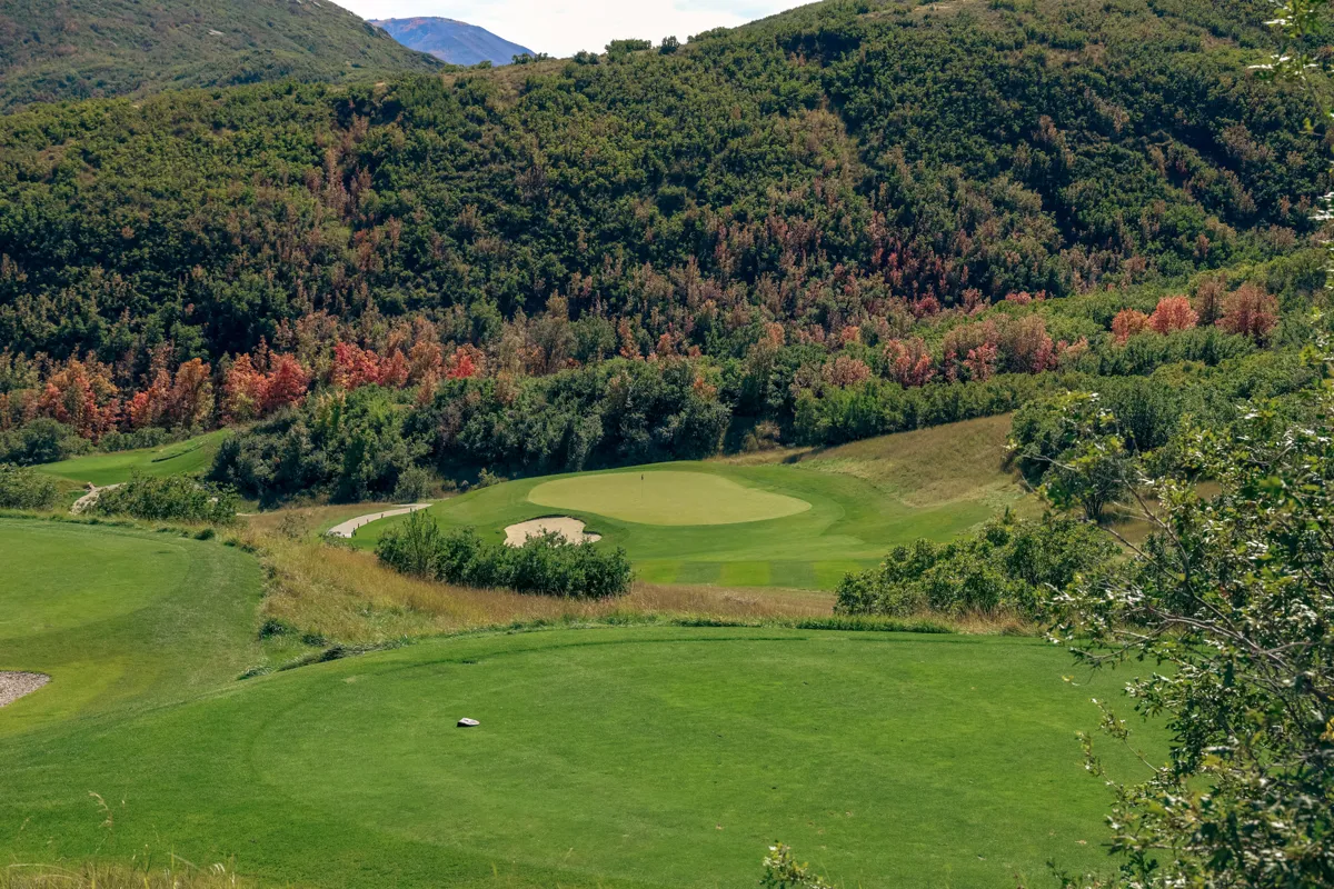 A par-3 green and bunkers on Soldier Hollow’s Gold Course, with wooded hills and autumn foliage beyond.