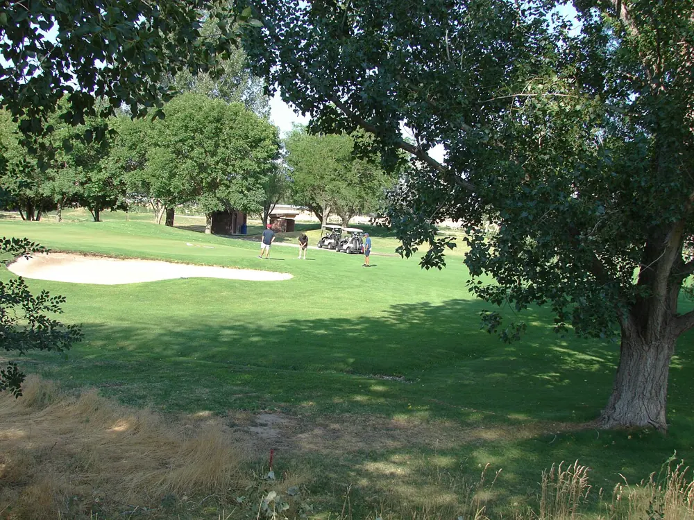 Golfers beside a green and bunker framed by trees at Spanish Oaks in Spanish Fork