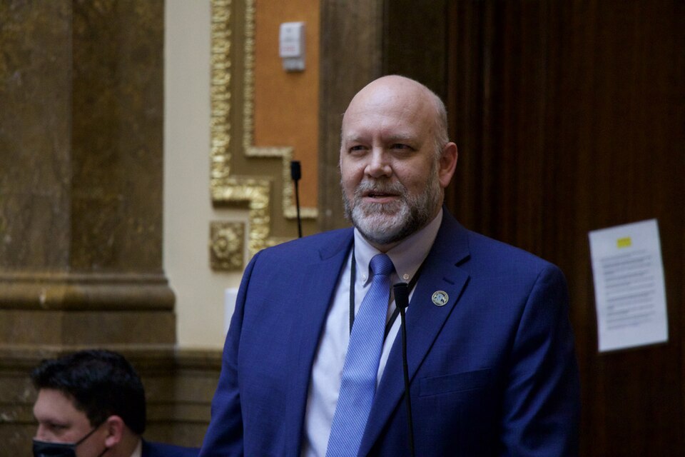 Doug Welton, wearing a blue suit and tie, stands at a microphone in the Utah House chamber.