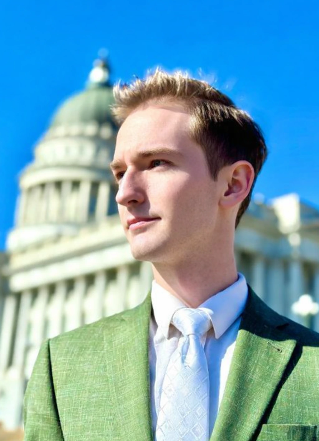 Elias Montgomery in a green suit and white tie outside the Utah State Capitol; campaign portrait.