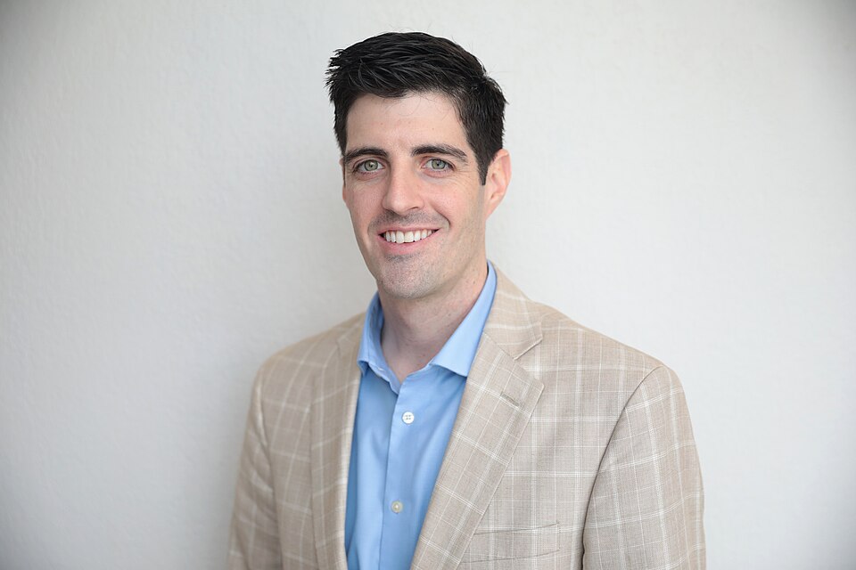 Jason Kyle smiling in a tan checked jacket and blue shirt.
