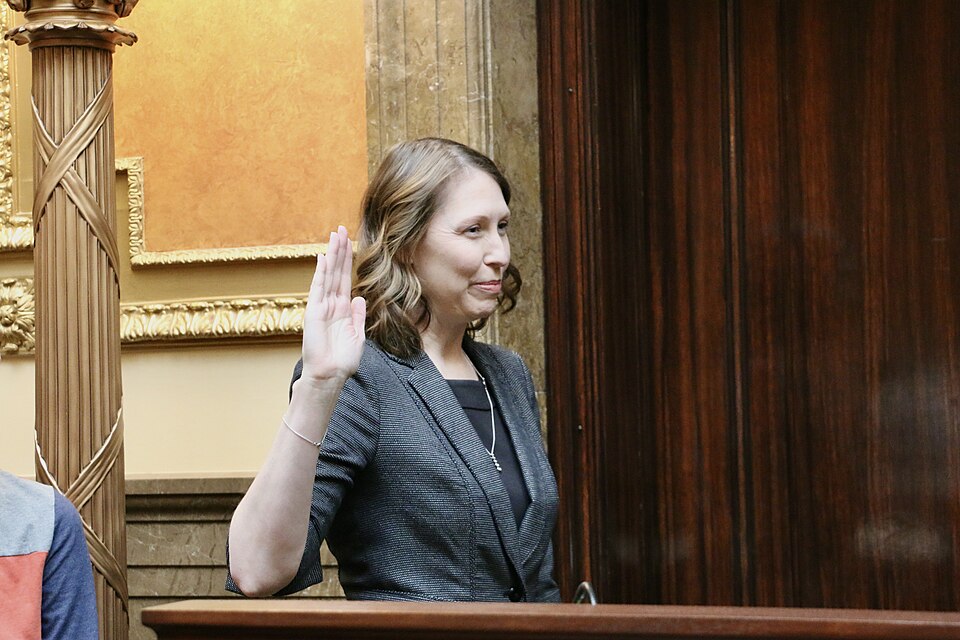 Karen Peterson raising her right hand beside a House podium.