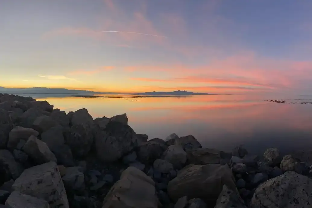 Shoreline rocks and calm Great Salt Lake water beneath a pink and orange sunset
