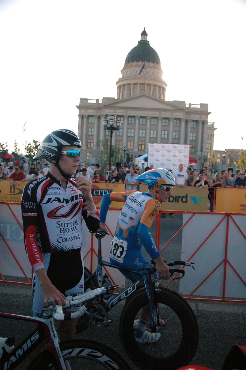 Two helmeted cyclists beside a barrier at a Tour of Utah event